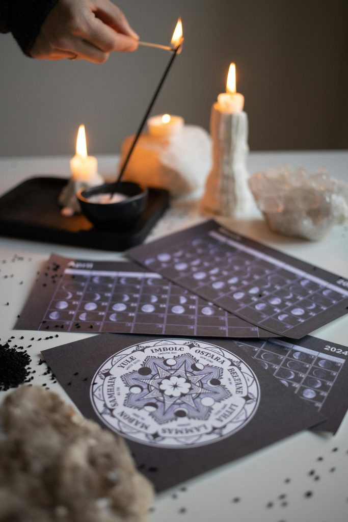 Mystical scene with a hand lighting an incense stick, lit candles, and a moon phase calendar.