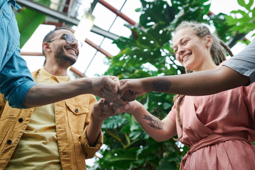 pexels photo 3228684 3228684 A group of young adults celebrating teamwork with a fist bump in a lush outdoor setting.